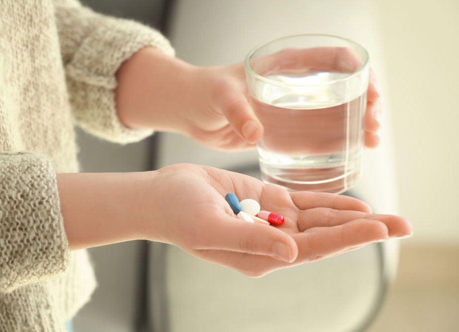 Woman holds pills in hand with glass of water in other hand