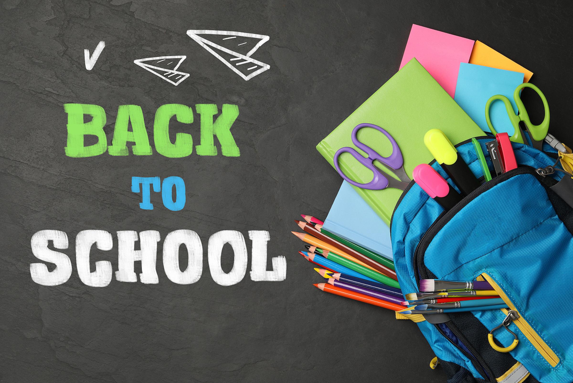 Back to school text on chalkboard next to backpack filled with school supplies.