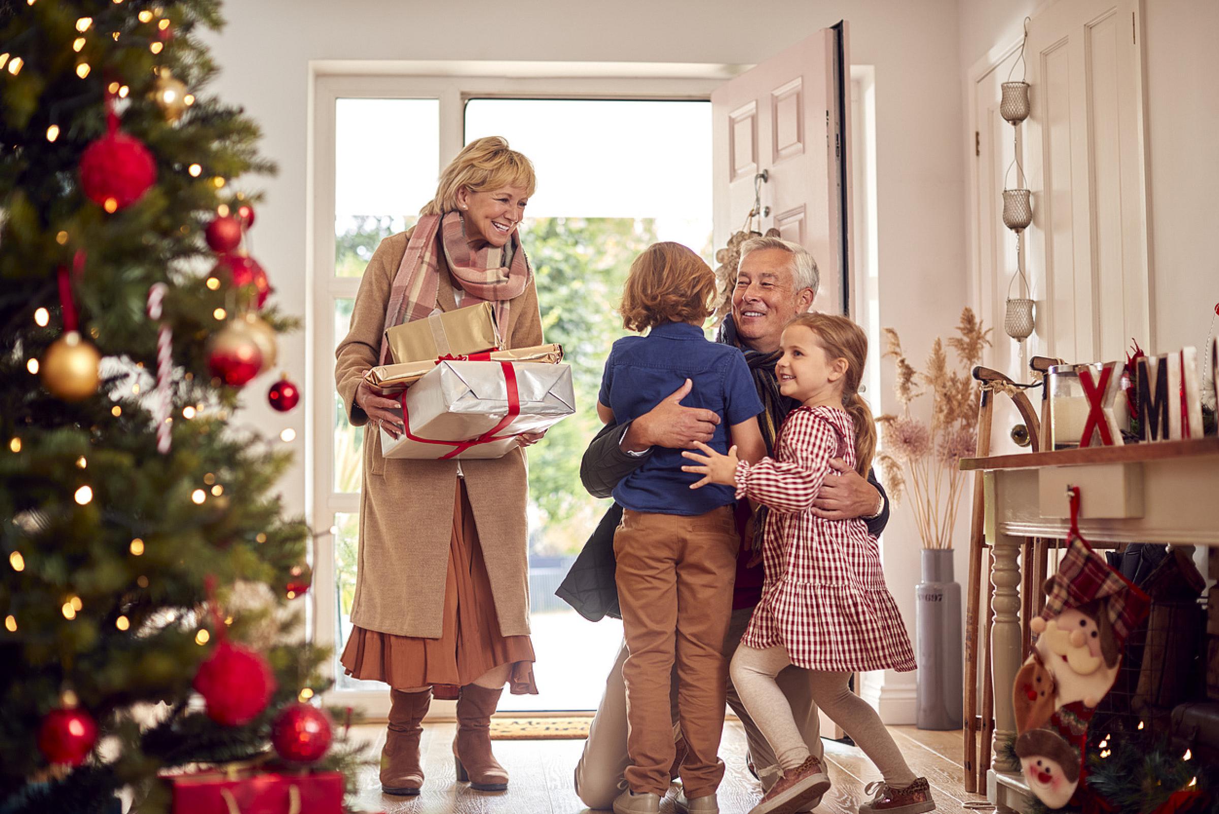 Grandparents visiting for Christmas meeting kids at front door with presents
