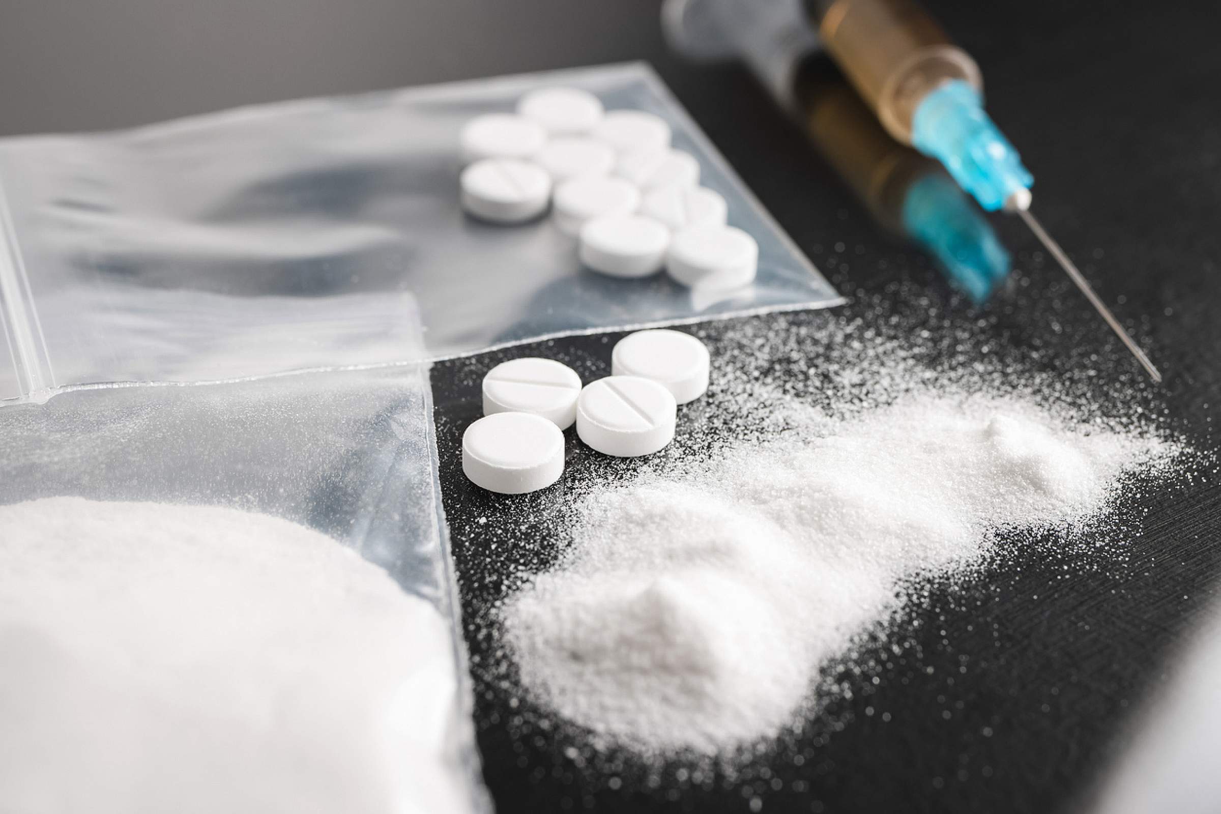 White powder, pills and syringe with needle on table; examples of illegal drugs that xylazine could be found in. 
