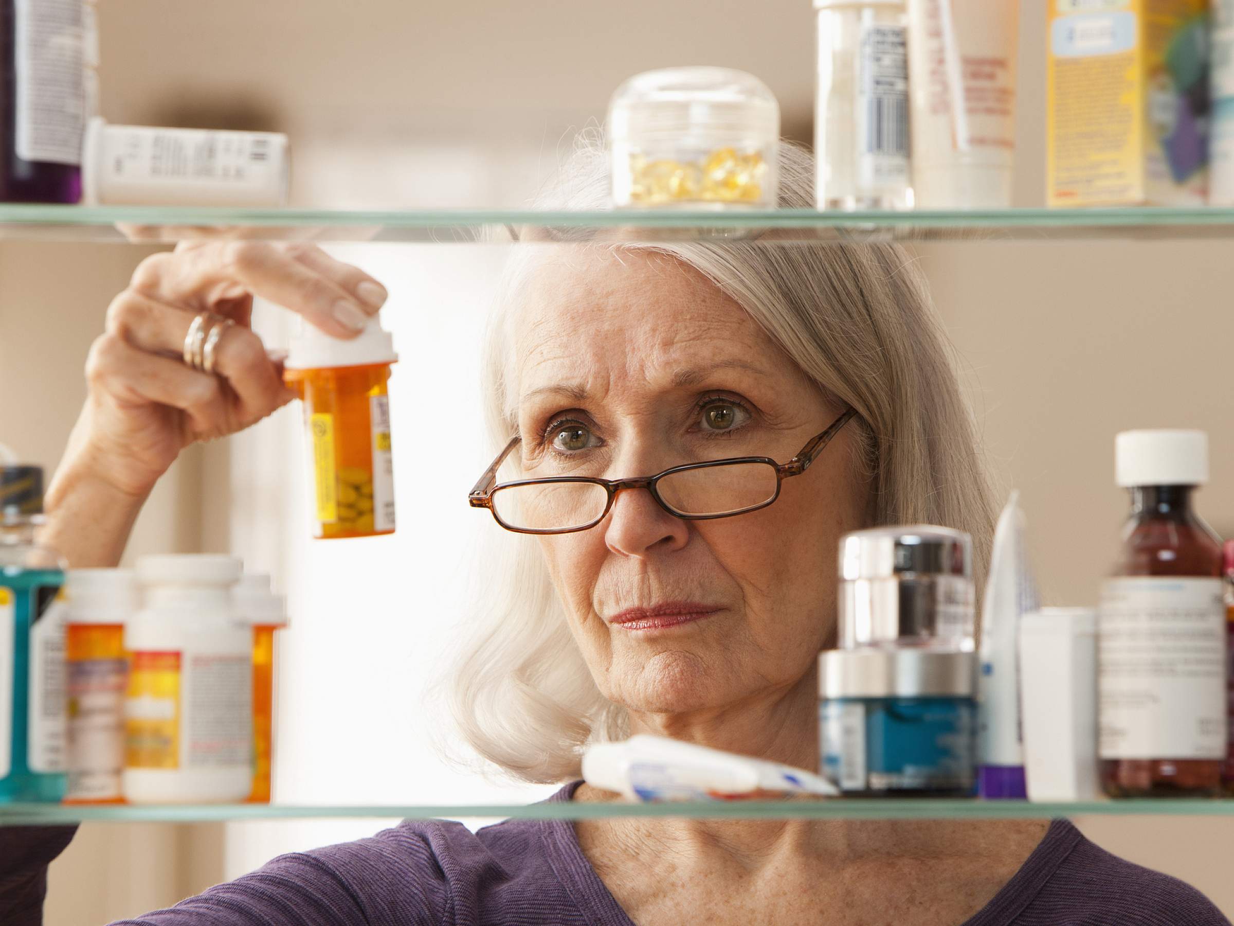 Senior woman reading prescription label through medicine cabinet.